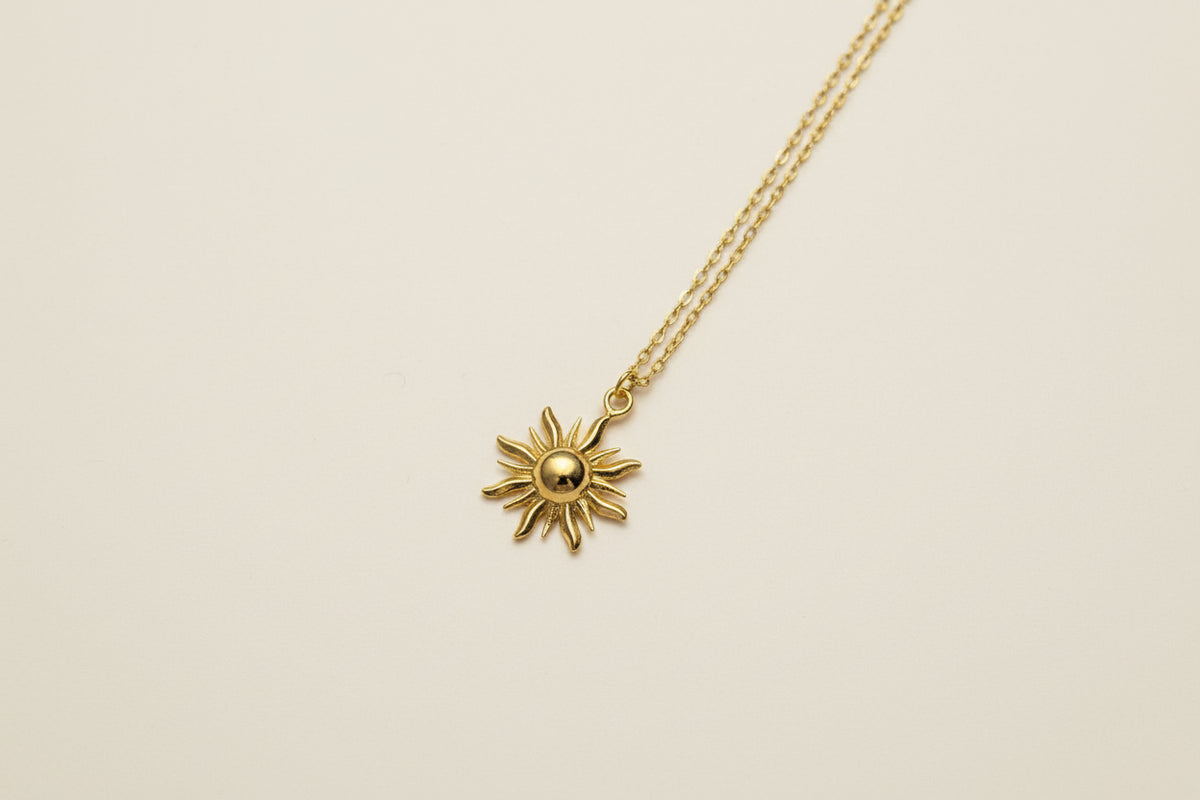 Gold sun-shaped pendant on a chain against a light beige background
