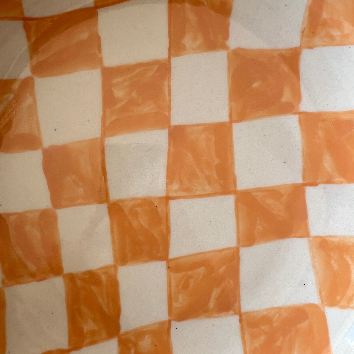 A close-up of a checkered pattern with alternating orange and off-white squares, showing a slightly textured surface.
