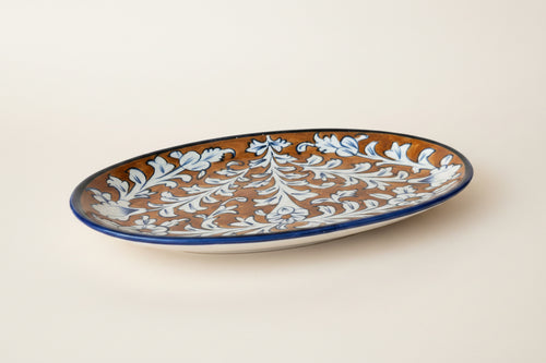 An oval ceramic serving platter with a brown and white floral pattern and a blue rim.