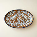 An oval ceramic serving platter with a brown glaze and a blue floral scroll pattern.