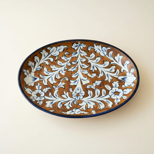 An oval ceramic serving platter with a brown glaze and a blue floral scroll pattern.