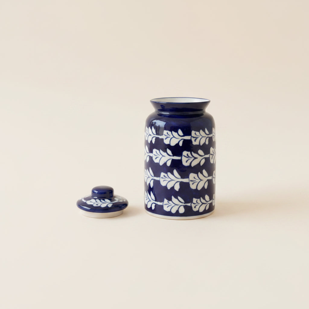 A cobalt blue ceramic jar with a matching lid, decorated with a white leaf pattern