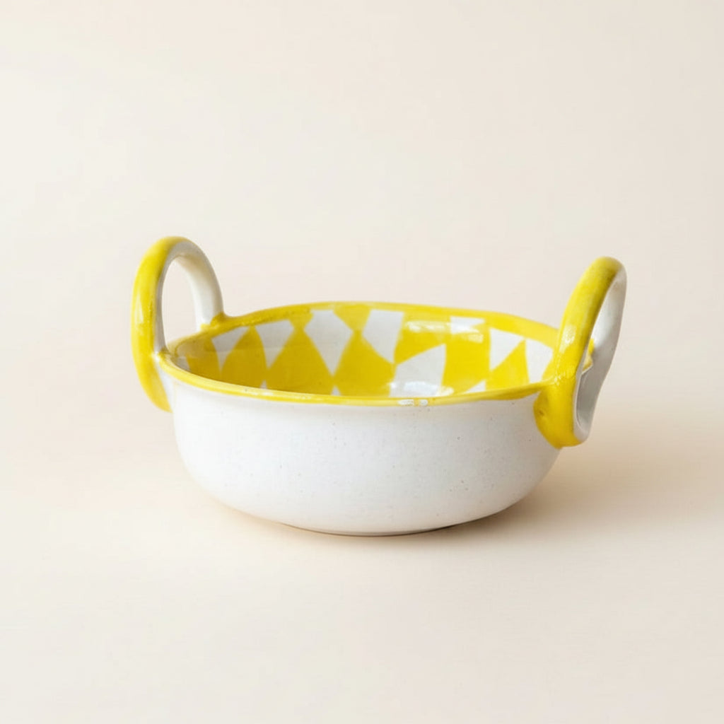 A small ceramic bowl with two loop handles, featuring a white speckled exterior and a yellow-and-white geometric patterned interior
