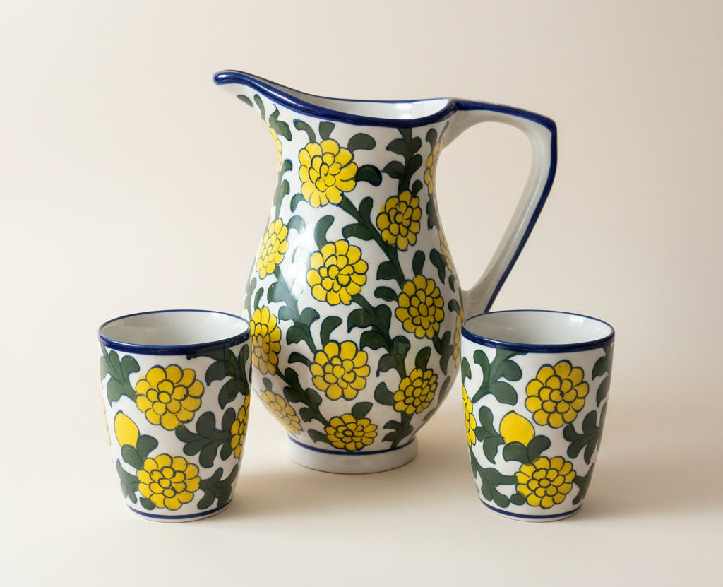 A ceramic pitcher and two matching cups with a yellow floral pattern on a white background.